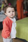 Portrait de bébé fille mignonne debout sur fond flou et regardant la caméra — Photo de stock