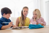 Mother and children doing homework on table — Stock Photo