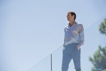 Homem em pé no terraço com cerca de vidro com as mãos nos bolsos — Fotografia de Stock