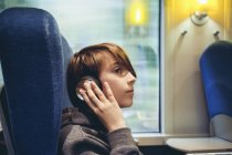 Niño escuchando música con auriculares en transporte público - foto de stock