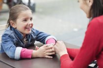 Улыбающаяся девушка сидит с мамой в кафе на тротуаре — стоковое фото