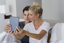 Casal jovem tomando selfie com tablet digital na cama — Fotografia de Stock