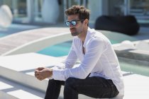 Nahaufnahme eines eleganten Mannes in weißem Hemd mit Sonnenbrille, der auf einer Treppe im Freien sitzt — Stockfoto