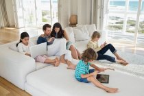 Famiglia utilizzando gadget elettronici in un soggiorno — Foto stock