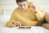 Frau im gelben flauschigen Pullover isst Schokoladenbonbons auf dem Bett — Stockfoto