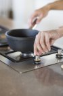 Mains féminines mettant casserole sur cuisinière à gaz dans la cuisine — Photo de stock