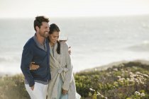 Sonriente abrazo pareja caminando en la costa del mar - foto de stock