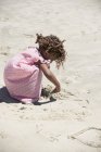 Маленькая девочка в розовом платье играет с песком на пляже — стоковое фото
