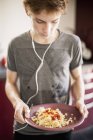 Teenage boy listening to music and holding plate of food — Stock Photo