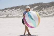 Glückliches kleines Mädchen spielt am Strand mit buntem Ball — Stockfoto