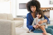 Mujer poniéndose calcetines a su hija y sonriendo - foto de stock