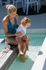 Bella donna seduta a bordo piscina con la sua bambina — Foto stock
