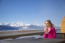 Woman drinking coffee on terrace with view of mountains, Crans-Montana, Swiss Alps, Switzerland — Stock Photo