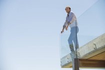 Мужчина стоит на террасе со стеклянным забором и смотрит в сторону — стоковое фото