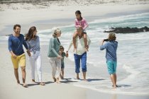 Мальчик фотографирует семью, гуляющую по песчаному пляжу — стоковое фото
