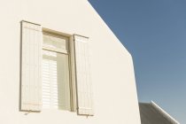 Window with roller blinds and white house facade against clear sky — Stock Photo