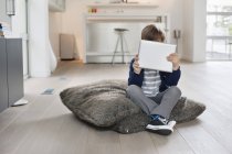 Cara de niño escondido con tableta digital en apartamento moderno - foto de stock