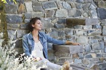Woman leaning against stone wall and day dreaming — Stock Photo