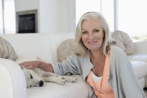 Портрет усміхається жінка, сидячи на канапі в домашніх умовах і гладила собака — стокове фото