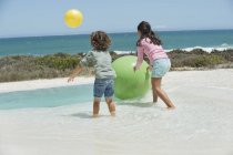 Fröhliche Kinder spielen am Sandstrand mit Bällen — Stockfoto