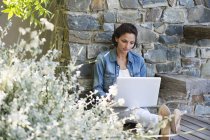 Frau lehnt an Steinmauer und benutzt Laptop — Stockfoto