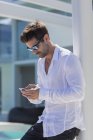 Крупный план человека в белой рубашке и солнцезащитных очках с использованием смартфона на улице — стоковое фото