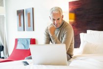 Homme mature utilisant un ordinateur portable dans la chambre d'hôtel — Photo de stock