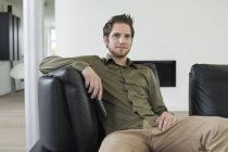 Positive young man watching television on sofa at home — Stock Photo