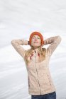 Femme détendue en bonnet tricoté avec les yeux fermés debout dans la neige — Photo de stock