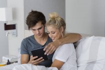 Молода пара обіймає з використанням цифрового планшета на ліжку — стокове фото