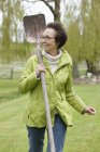 Sorrindo mulher sênior andando com pá no parque e olhando para longe — Fotografia de Stock
