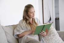 Mulher focada leitura livro no sofá em casa — Fotografia de Stock