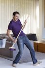 Man holding mop as guitar in living room — Stock Photo