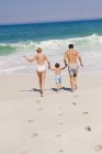 Семья бежит по песчаному пляжу держа за руки — стоковое фото