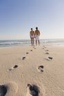 Huellas en la playa de arena con la pareja de pie sobre el fondo y mirando a la vista - foto de stock