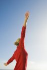 Femme en pull rouge étirant les bras contre le ciel bleu — Photo de stock