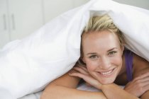 Gros plan de la femme couchée sur le lit sous la couette et souriante — Photo de stock