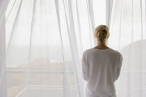 Visão traseira da mulher cortina de abertura da varanda em casa — Fotografia de Stock