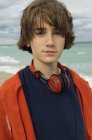 Portrait of teenage boy with headphones standing on sea beach — Stock Photo