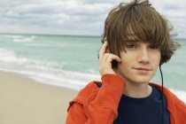 Portrait de garçon écoutant des écouteurs sur la plage sous un ciel nuageux — Photo de stock