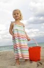 Petite fille mignonne tenant seau de sable sur la plage — Photo de stock
