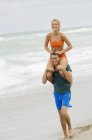 Homem carregando mulher nos ombros na praia — Fotografia de Stock
