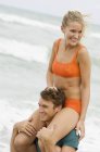 Man carrying woman on shoulders on beach — Stock Photo