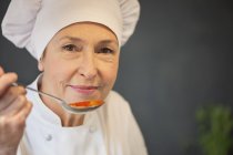 Portrait of woman in chef costume tasting tomato sauce — Stock Photo
