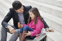 Man sitting on stairs with daughter and eating pain au chocolat — Stock Photo