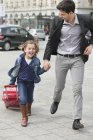 Girl pulling trolley bag while running with father on street — Stock Photo