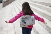 Rear view of little girl with backpack walking on steps — Stock Photo
