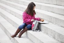 Дівчина бере їжу зі шкільної сумки, сидячи на сходах — стокове фото