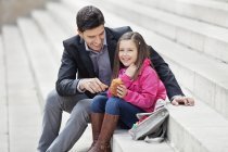 Man sitting on stairs with daughter and eating pain au chocolat — Stock Photo