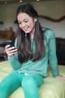 Портрет улыбающейся девушки с помощью мобильного телефона на кровати — стоковое фото